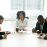 Businessman and businesswoman signing contracts at group multiracial meeting, two smiling male and female new partners signing papers after a mediation