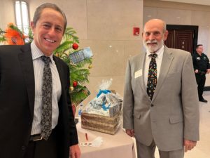 Mediators Eric Luckman and Jose G. Rodriguez stand by the firm's gift basket donation for the Annual Holiday Party 