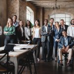 A group of multigenerational and disabled work colleagues standing in an office conference room.