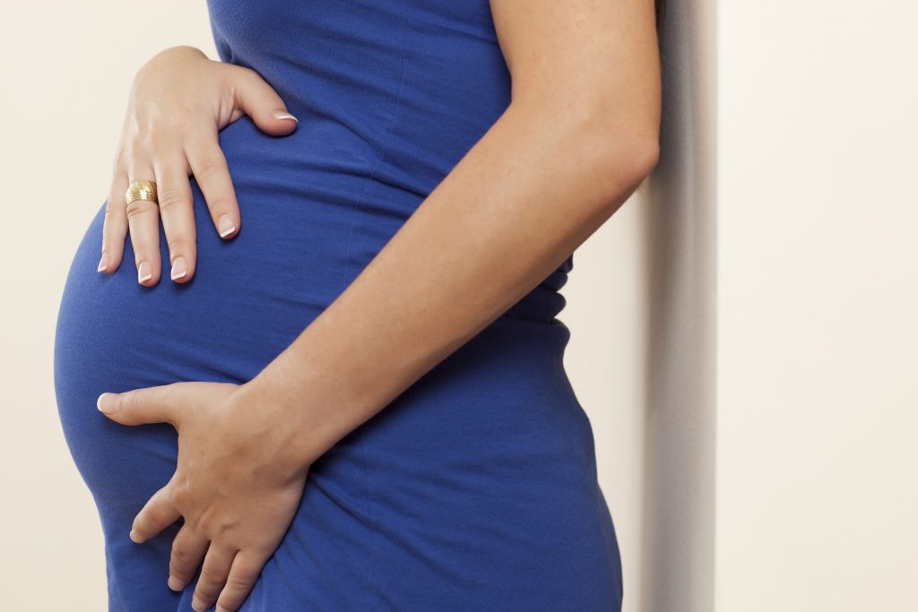 Pregnant women in a blue dress with hands on her belly