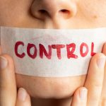 Control your tongue. Female holding plastered tape and covering her lips. Power of words, freedom of speech, silence, and communication concept. A close-up.